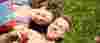Teenage boy and girl holding hands, smiling, laying on grass together