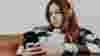 A teen girl sits on the sofa looking at her phone with headphones on